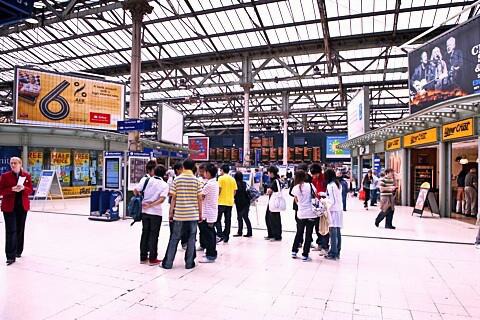 Photo of a busy train station concourse with people gathered and moving through the space, reflecting daily travel and community activity