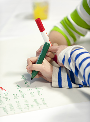 Photo of a piece of paper with writing, with hands holding green and red marker pens, representing learning and classroom activities