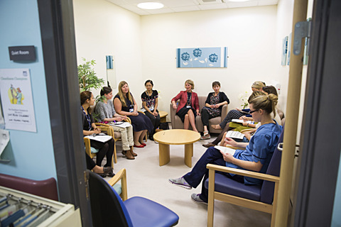 Photo of a multidisciplinary team meeting viewed through a doorway, showing staff seated around the room in active discussion